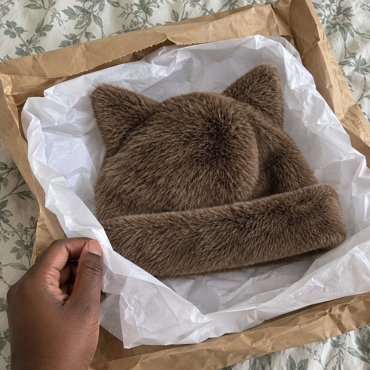 Illustrative photo of a hand unwrapping a Coffee Cleo cat ear hat from its shipping mailer.