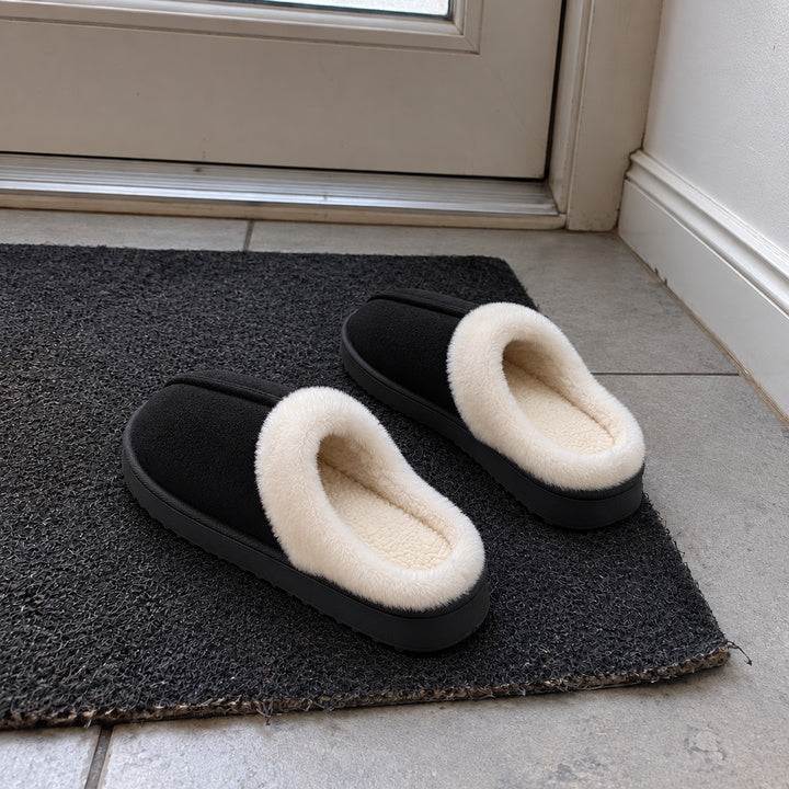 An empty Black pair of Haven slippers on a doormat, viewed from behind.