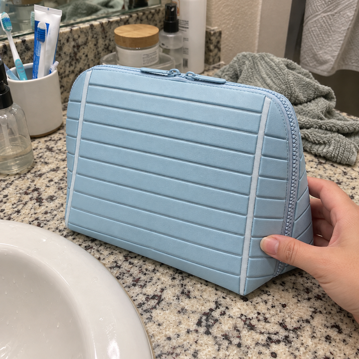 A hand steadies closed Light Blue Clara beside a bathroom sink