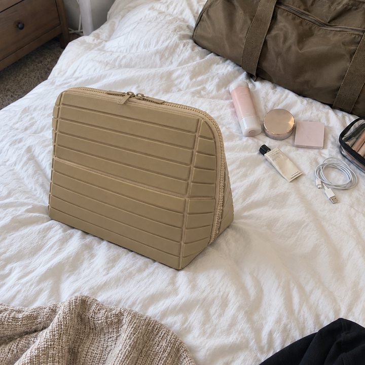 Closed Apricot Clara on a rumpled bed beside a weekender and toiletries