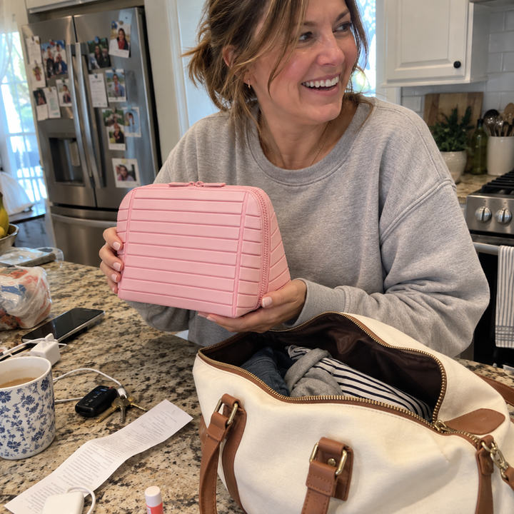 Woman holding closed Pink Clara beside an open weekender in a kitchen