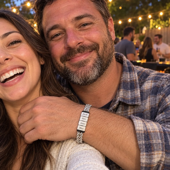 A woman's front-camera selfie with her husband at a backyard barbecue, his arm around her and the silver Harbor name bracelet with four names on his wrist, everyday phone photo