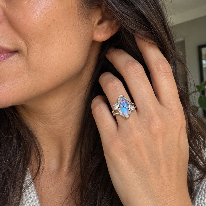 Hand tucking hair behind an ear, the simulated moonstone ring on the ring finger