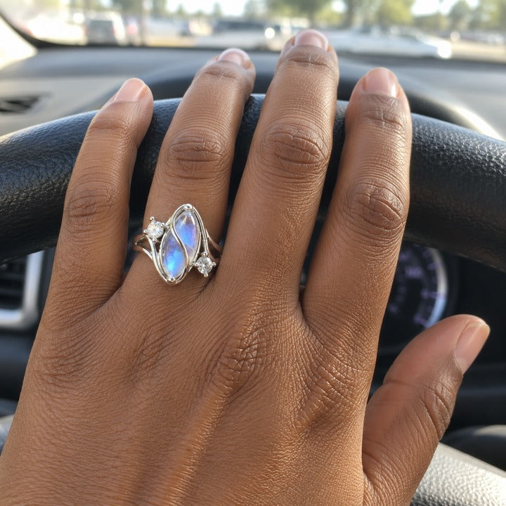 Hand over the top of a car's steering wheel, wearing the simulated moonstone ring