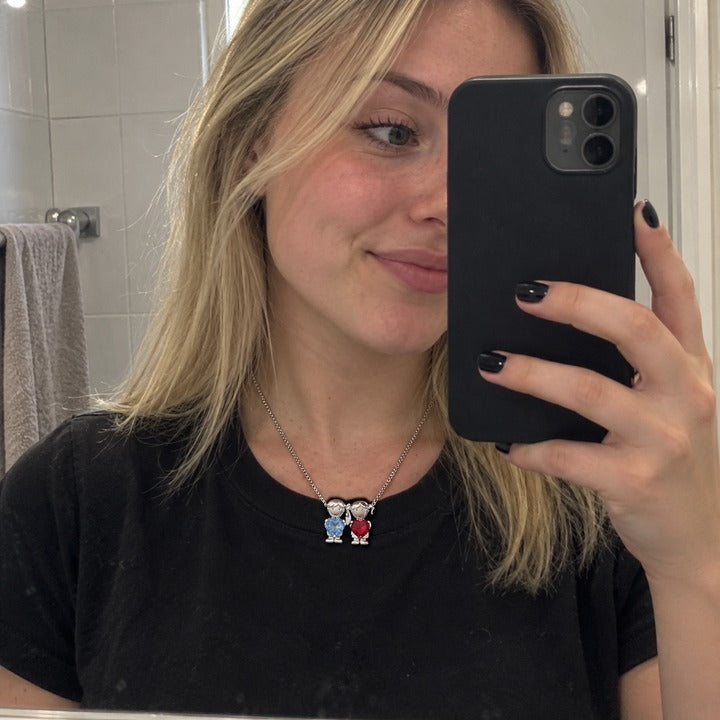 Mirror selfie with her phone, the silver-tone necklace's boy and girl charms in sky blue and deep red on a black tee