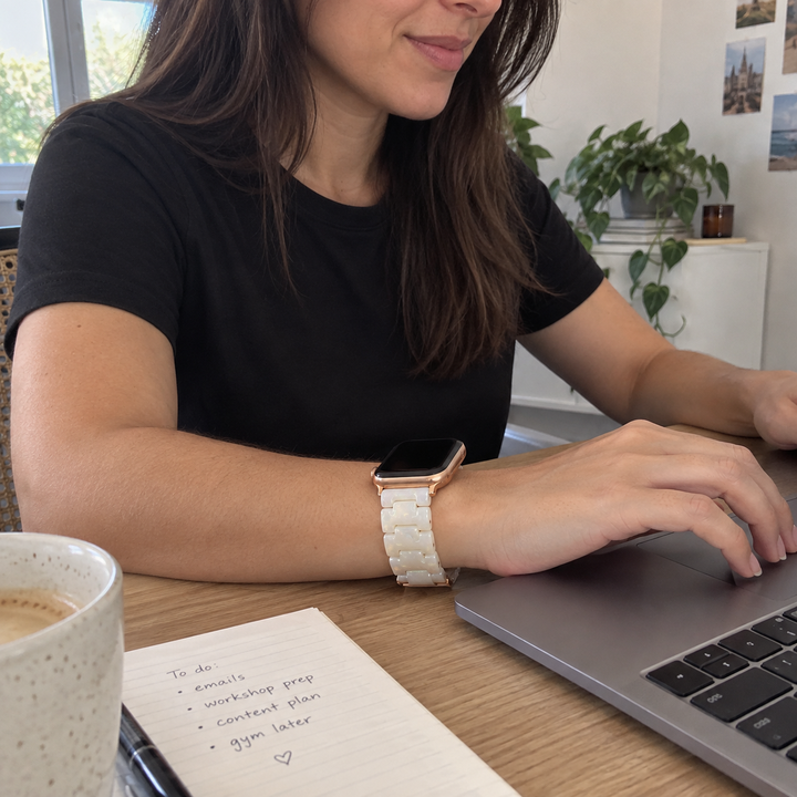 Woman wearing an Adirena resin link watch band in Opal White, at a desk mid-typing