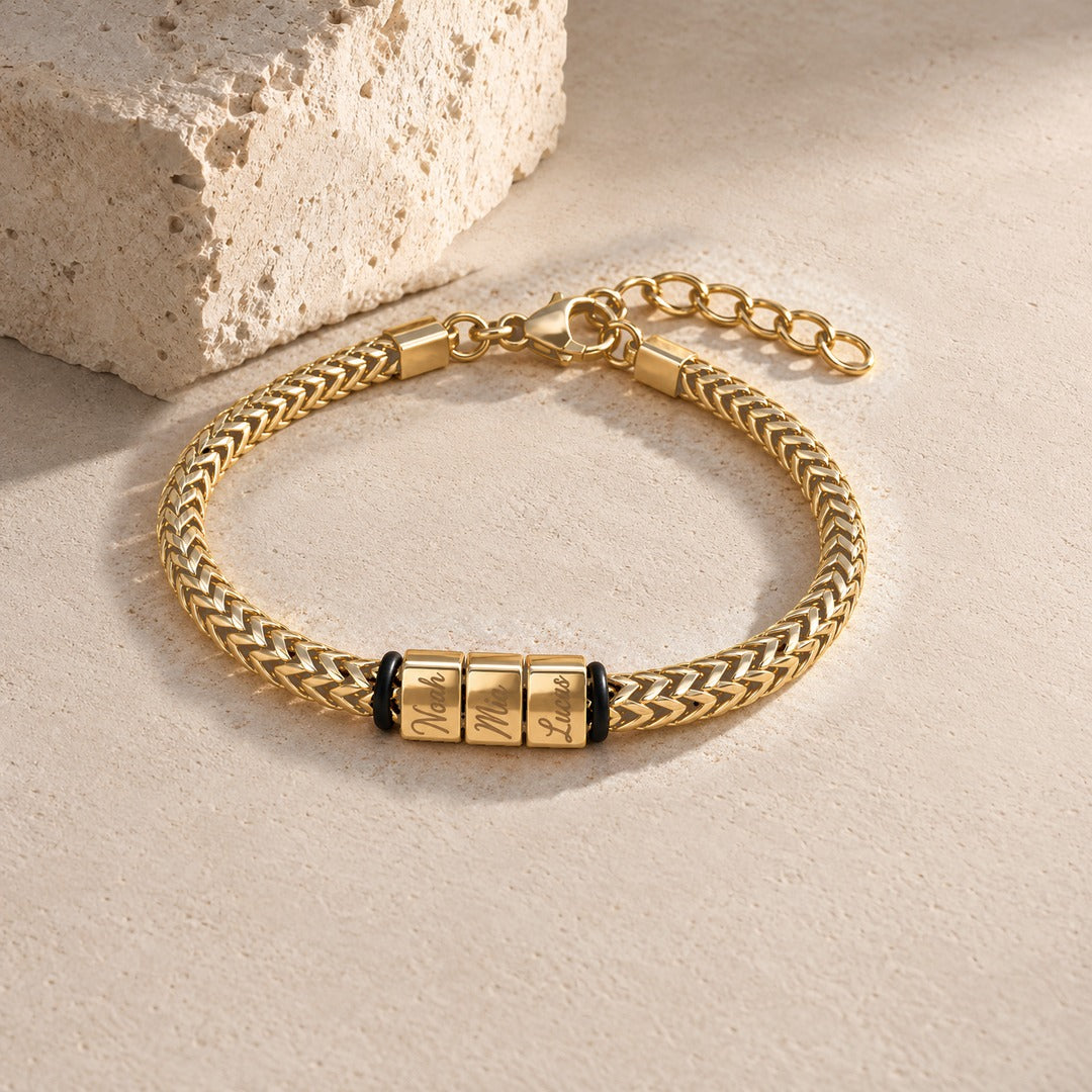 Harbor name bracelet in gold with three engraved name blocks, laid on pale stone