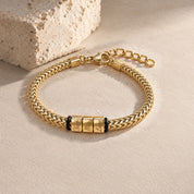 Harbor name bracelet in gold with three engraved name blocks, laid on pale stone