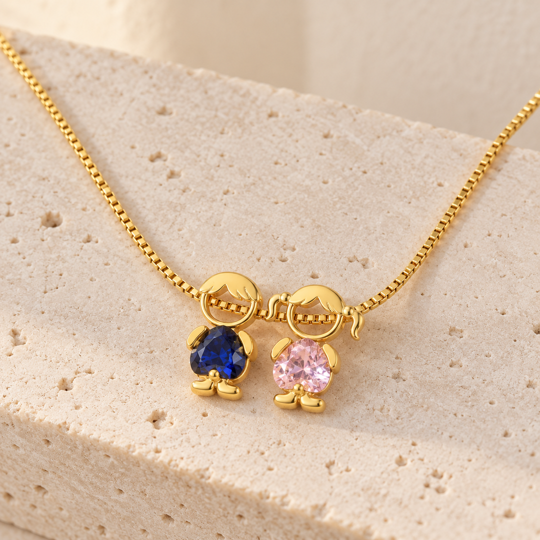 Gold-tone necklace on pale travertine with a boy and a girl charm, a royal blue and a pale pink heart-cut stone
