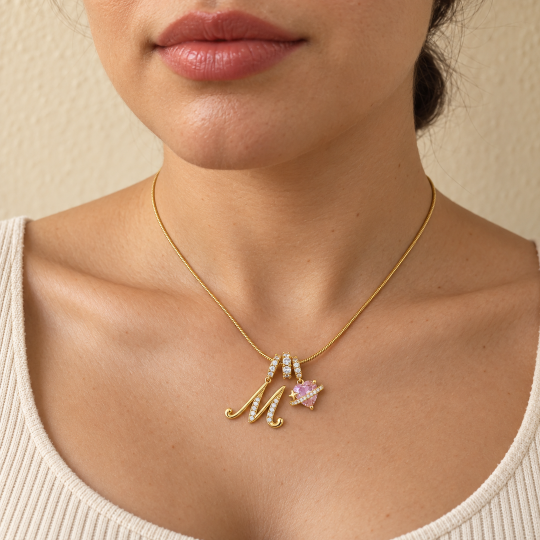 Cherie initial necklace in gold worn at the base of the neck, initial M and pink heart