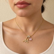 Cherie initial necklace in gold worn at the base of the neck, initial M and pink heart