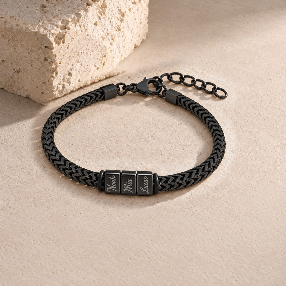 Harbor name bracelet in black with three engraved name blocks, laid on pale stone