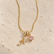 The gold Cherie initial necklace with initial A, its three stone-set rings and the pink heart on travertine