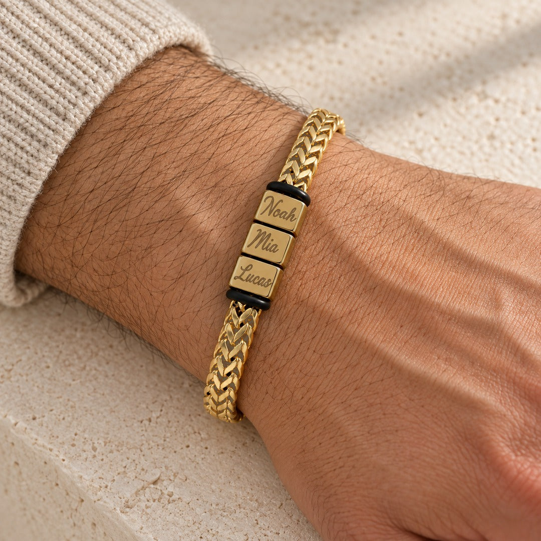 The gold Harbor name bracelet on a man's wrist, three engraved names, a cream knit cuff