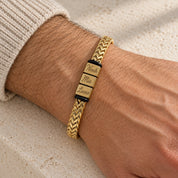 The gold Harbor name bracelet on a man's wrist, three engraved names, a cream knit cuff