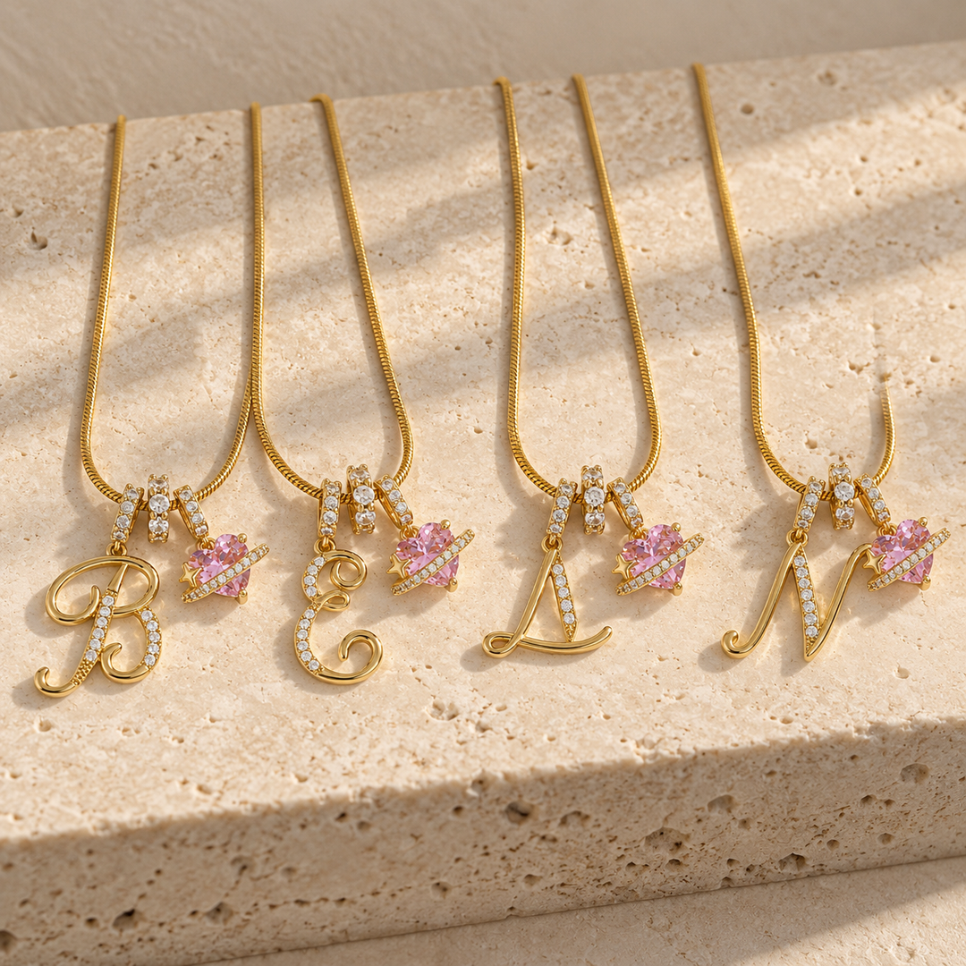 Four Cherie initial necklaces in gold on a travertine block, initials B, E, L and N