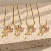 Four Cherie initial necklaces in gold on a travertine block, initials B, E, L and N