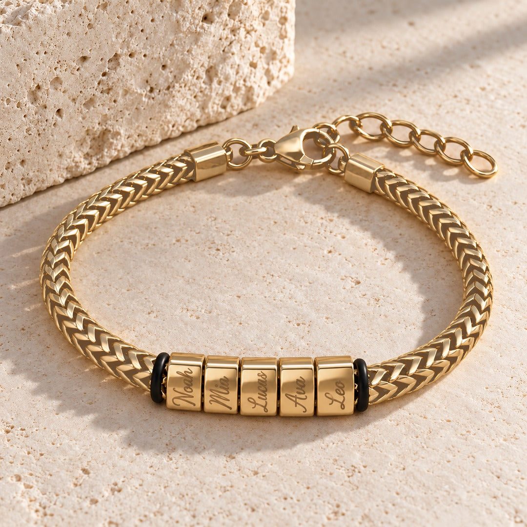 Gold Harbor name bracelet with five engraved name blocks, laid on pale stone