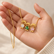 The gold-tone necklace in an open palm, three charms face up with clear, green and pale pink heart-cut stones