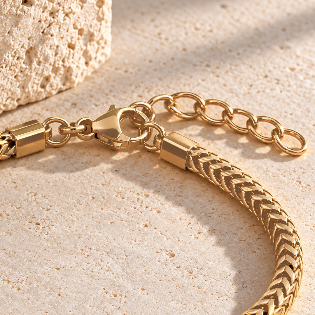 Lobster clasp, end caps and extender chain of the gold Harbor name bracelet on pale stone