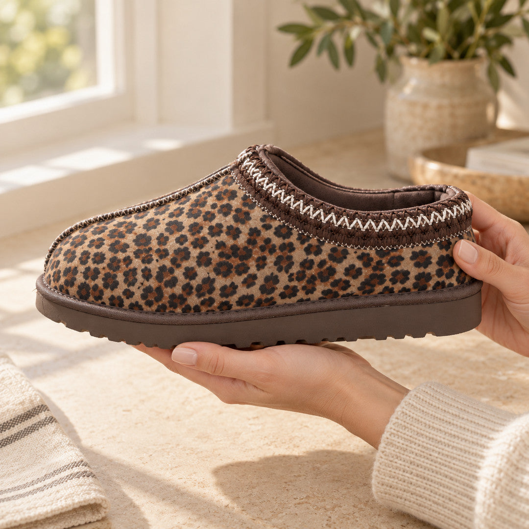 Hands holding a Thin Leopard Aspen slipper in side view, showing its stitched collar and brown sole.