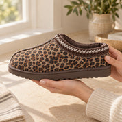 Hands holding a Thin Leopard Aspen slipper in side view, showing its stitched collar and brown sole.
