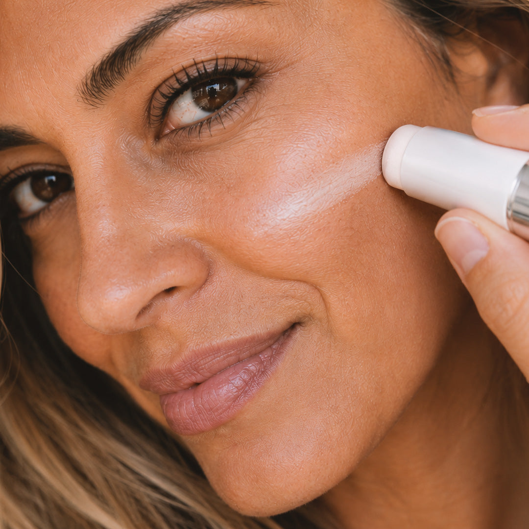 Woman applying Adirena Cover Cream stick, white swatch warming on cheek