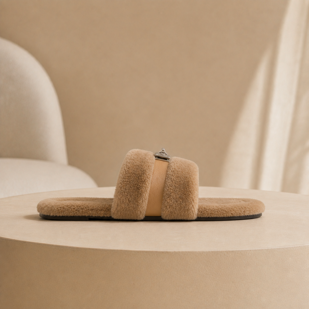 Side view of one taupe fur slipper showing the open back, the two fur bands and the metal buckle on its strap