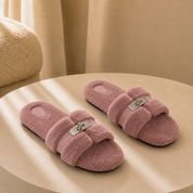 A pair of blush pink fur slippers on a warm plaster plinth