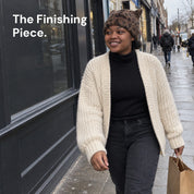A woman shopping on a city street in a Leopard Cleo cat ear hat and a cream knit cardigan, carrying a paper bag.