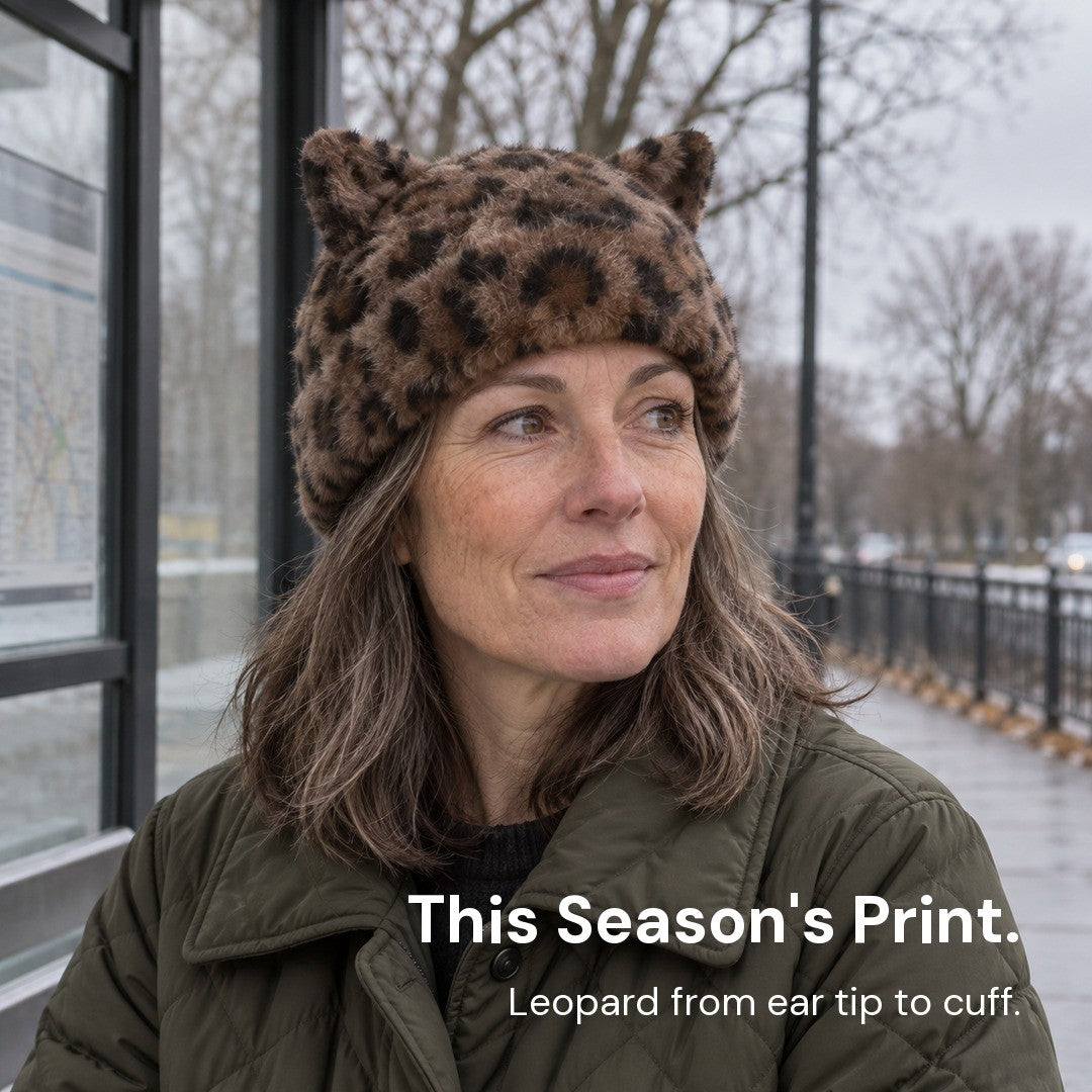 Woman in the Leopard Cleo cat ear hat and a quilted jacket waiting at a bus stop on a gray winter day.