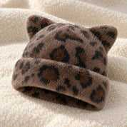 The Leopard Cleo cat ear hat laid on a cream knit throw.