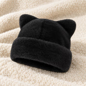 The Black Cleo cat ear hat laid on a cream knit throw.