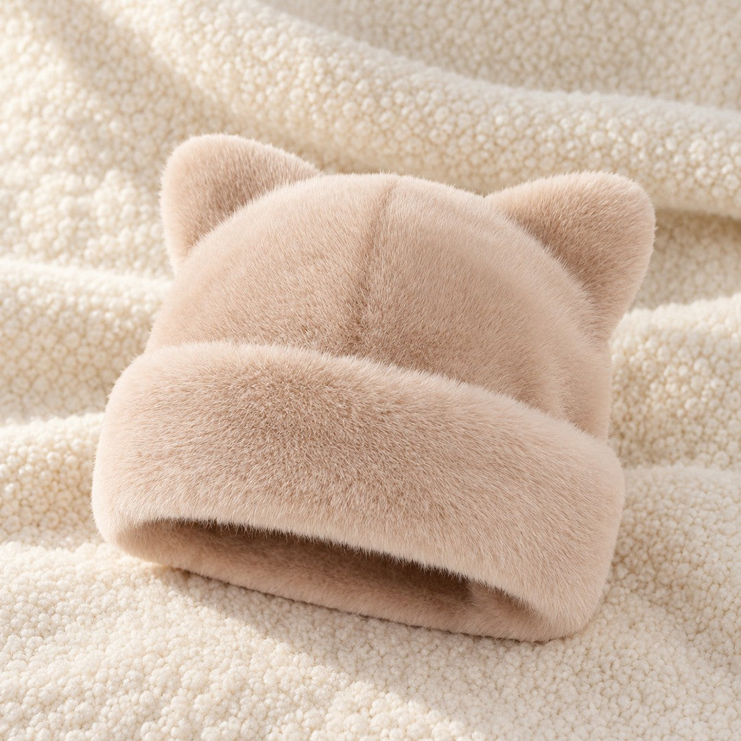 The Apricot Cleo cat ear hat laid on a cream knit throw.