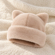 The Apricot Cleo cat ear hat laid on a cream knit throw.