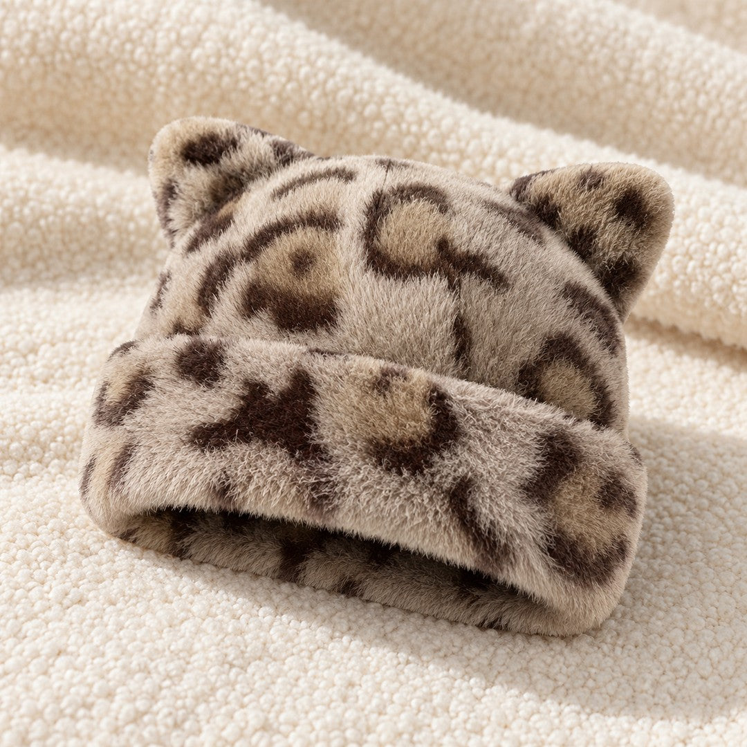 The Khaki Leopard Cleo cat ear hat laid on a cream knit throw.