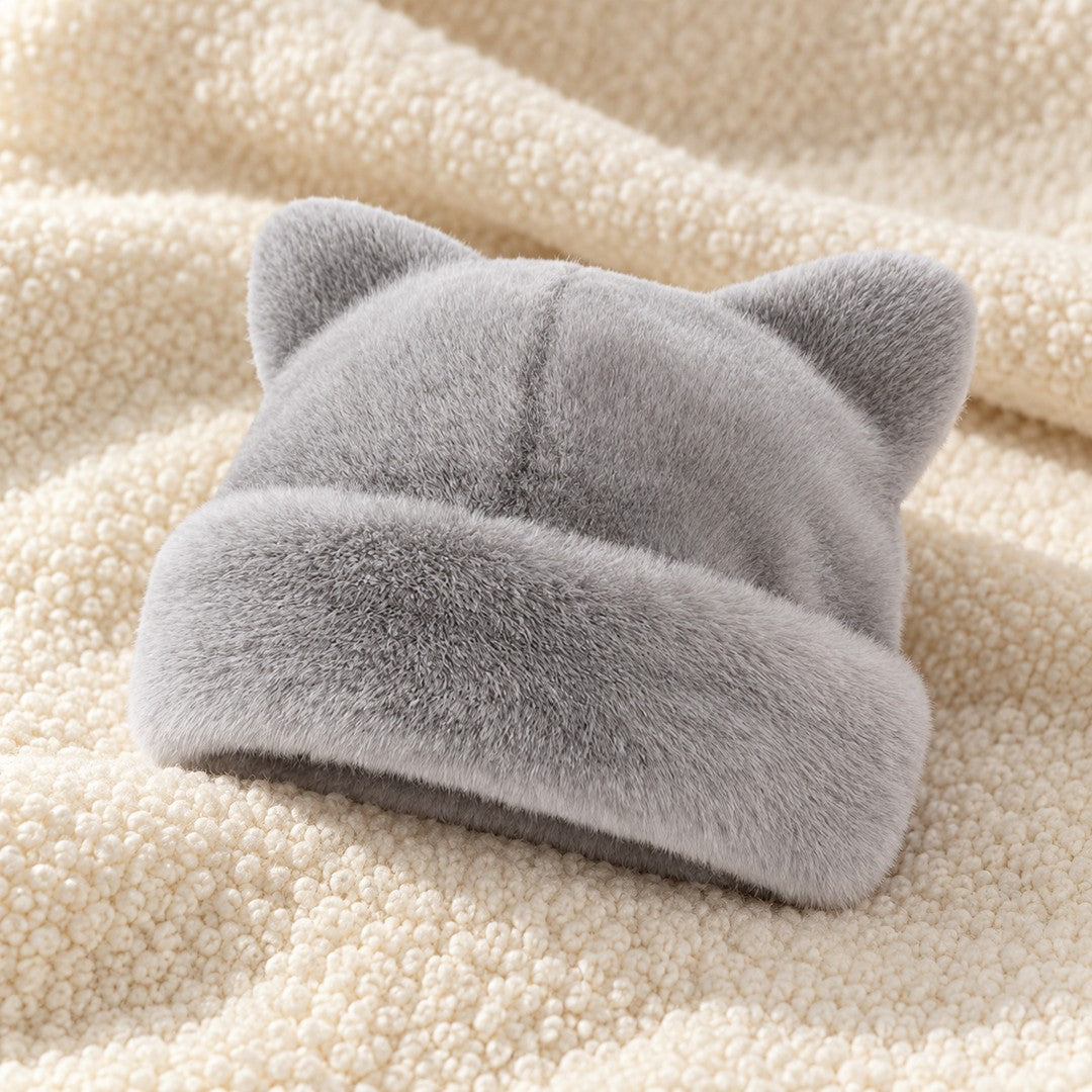 The Gray Cleo cat ear hat laid on a cream knit throw.