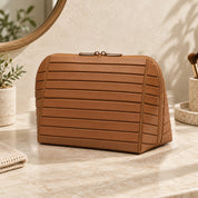 Closed brown Clara makeup bag viewed from the front on a warm vanity