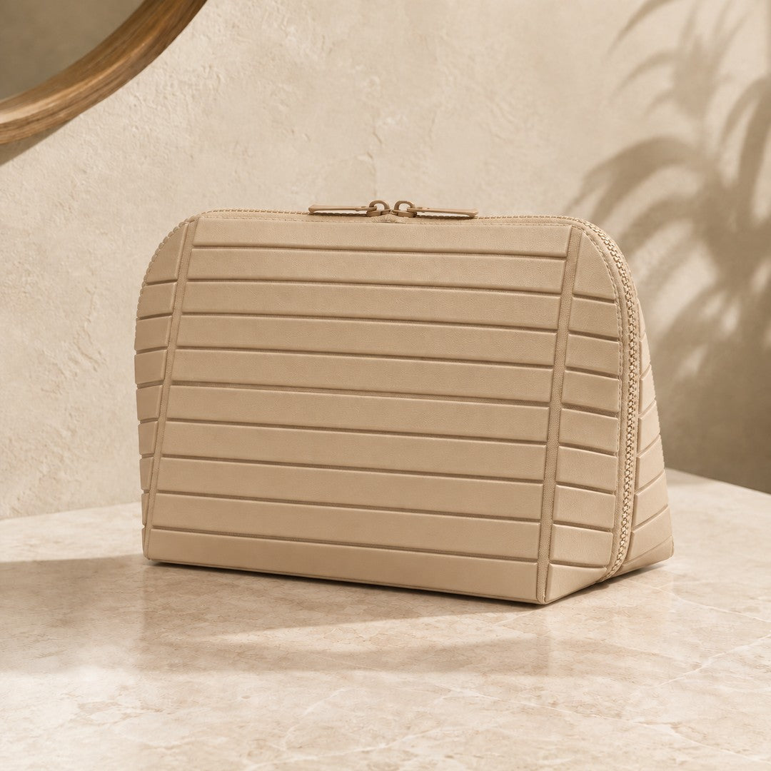 Closed apricot Clara makeup bag on a warm vanity, showing its broad face and right edge
