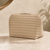Closed apricot Clara makeup bag on a warm vanity, showing its broad face and right edge