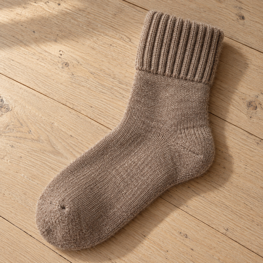 A single ribbed mid-calf sock lying on a warm floor, its knit heel pocket, rounded closed toe and folded cuff all visible