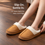 Chestnut Haven slippers worn on a dark wood floor, with fingertips beside the open back of the nearer slipper.