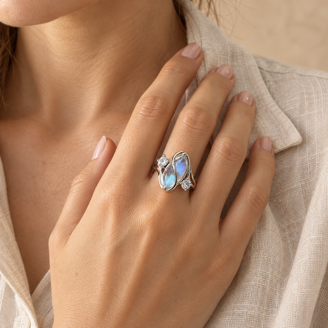 Hand at the collar of an oat linen shirt wearing the simulated moonstone ring on the ring finger