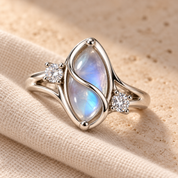 Front view of the ring in a fold of oat linen: marquise simulated moonstone, crossing wire and two side stones
