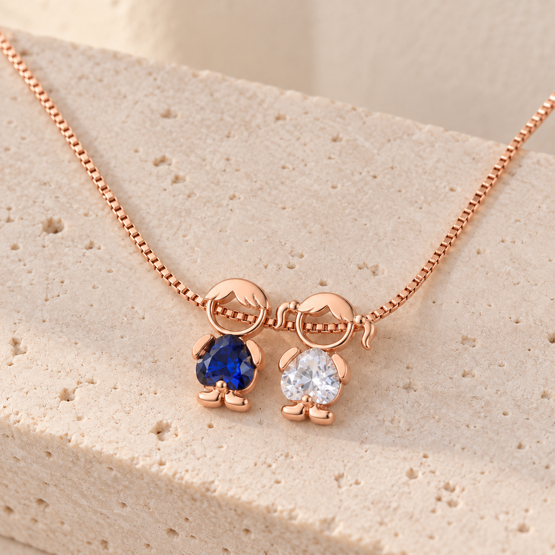 Rose gold-tone necklace on travertine with a boy and a girl charm, a royal blue and a clear heart-cut stone
