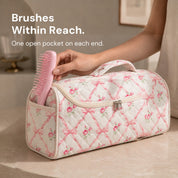 A hand lifting a pink hairbrush from the narrow end pocket of the Rose Lattice Sloane bag