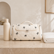 A cream quilted hair-tool case on a stone bathroom shelf beside a shampoo bottle and a folded towel