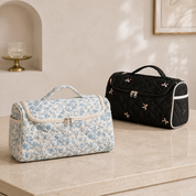 Two quilted hair-tool cases side by side on a pale stone shelf, one in blue floral and one in black with embroidered bows