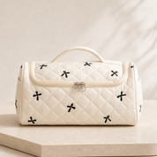 A cream quilted hair-tool case closed and seen straight on, showing its curved zip line and top handle