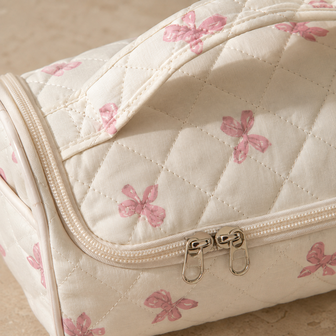 Close-up of the two silver zip sliders and the stitched-down handle on a quilted hair-tool case